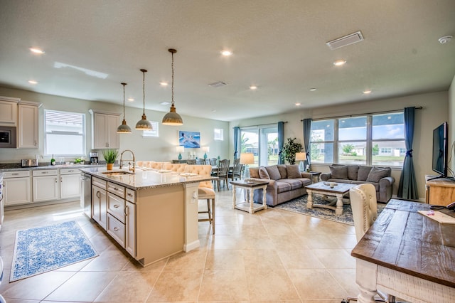 kitchen with pendant lighting, a kitchen bar, a kitchen island with sink, light stone counters, and stainless steel appliances