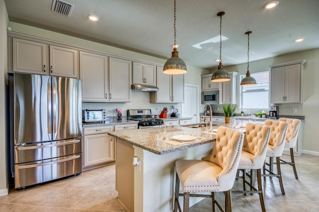 kitchen featuring sink, a breakfast bar area, stainless steel appliances, light stone countertops, and a center island with sink