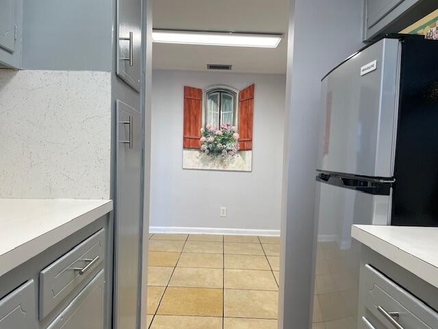 kitchen featuring backsplash, stainless steel fridge, light tile patterned floors, and gray cabinetry