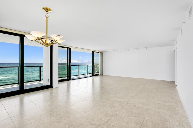 spare room featuring expansive windows, a water view, rail lighting, and a notable chandelier