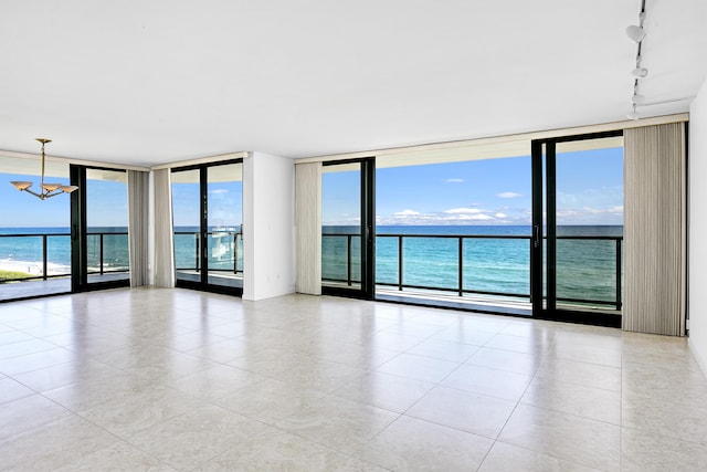 tiled spare room with rail lighting, a wealth of natural light, floor to ceiling windows, and a water view