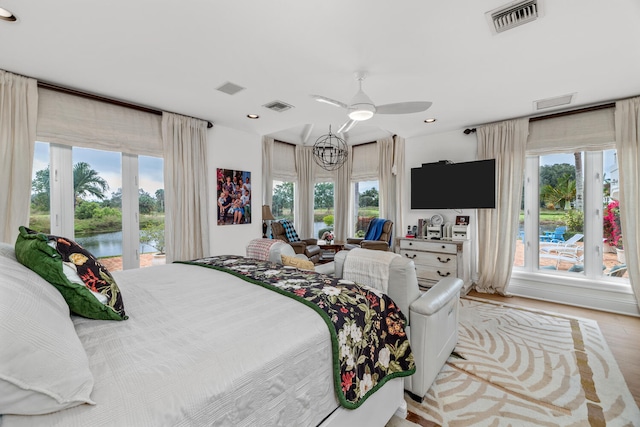 bedroom with multiple windows, access to exterior, light hardwood / wood-style flooring, and a water view