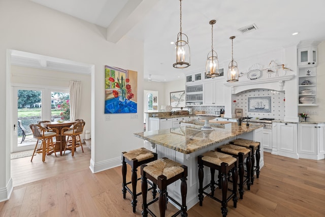 kitchen with white cabinetry, hanging light fixtures, a kitchen island with sink, light hardwood / wood-style floors, and light stone countertops