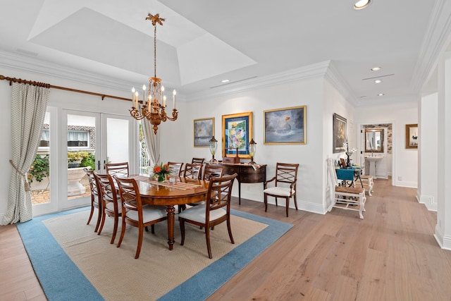 dining area featuring an inviting chandelier, ornamental molding, light hardwood / wood-style floors, and a raised ceiling