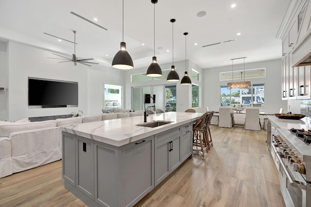 kitchen with a large island, sink, gray cabinetry, light stone counters, and decorative light fixtures