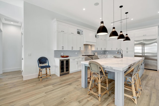 kitchen featuring decorative light fixtures, a large island with sink, stainless steel appliances, light stone countertops, and white cabinets