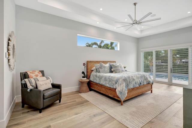 bedroom with access to exterior, light hardwood / wood-style flooring, a raised ceiling, and ceiling fan