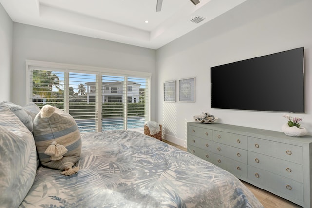 bedroom featuring light hardwood / wood-style flooring, a tray ceiling, access to outside, and ceiling fan