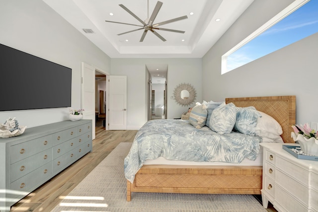 bedroom with ceiling fan, light wood-type flooring, and a tray ceiling