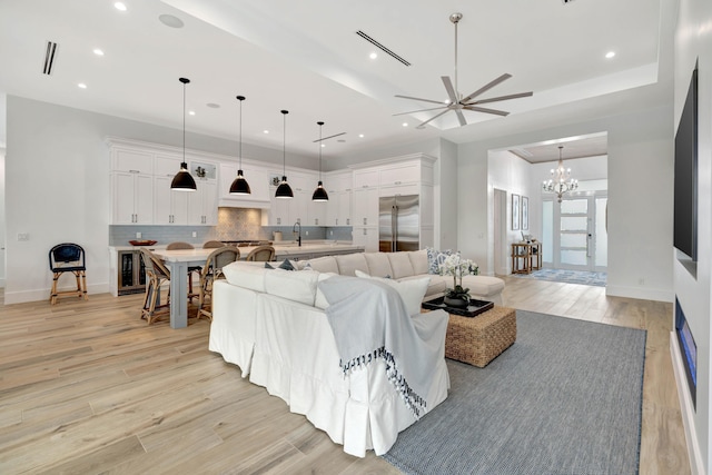 living room featuring ceiling fan with notable chandelier, sink, and light hardwood / wood-style flooring