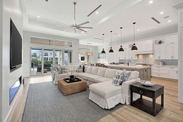 living room featuring ceiling fan, a towering ceiling, sink, and light wood-type flooring