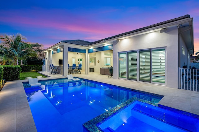 pool at dusk with a patio area, an outdoor bar, ceiling fan, and an in ground hot tub