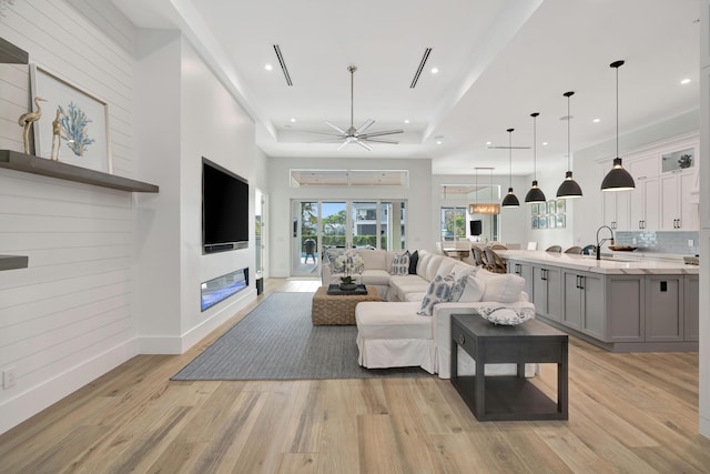 living room featuring sink, a tray ceiling, light hardwood / wood-style flooring, and ceiling fan