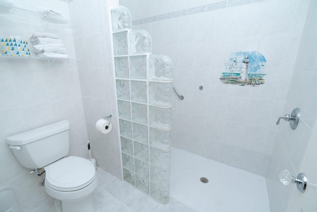 bathroom featuring tile patterned floors, toilet, tile walls, and a tile shower