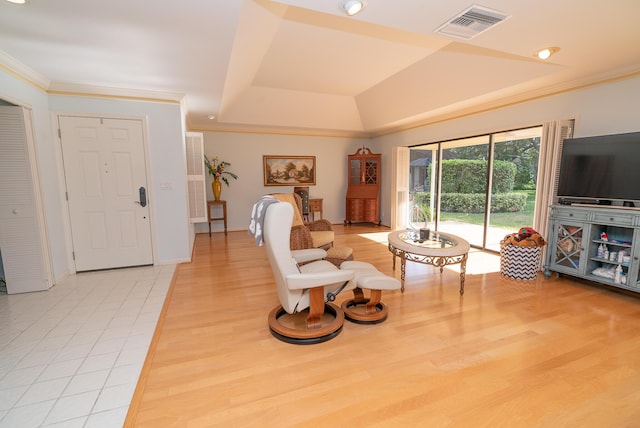 living room with a raised ceiling, crown molding, and light wood-type flooring