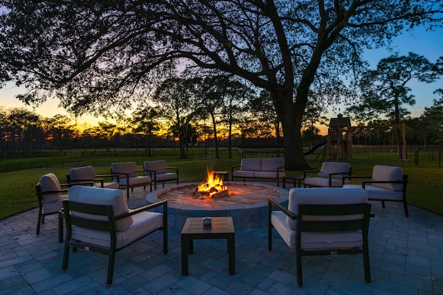 patio terrace at dusk featuring a playground, an outdoor living space with a fire pit, and a lawn