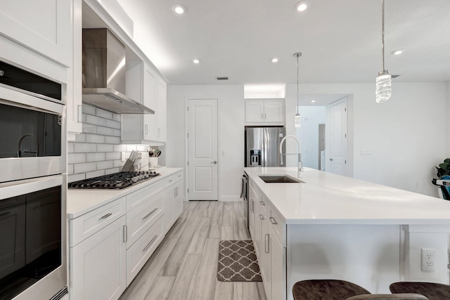 kitchen with pendant lighting, appliances with stainless steel finishes, white cabinetry, a kitchen breakfast bar, and wall chimney exhaust hood