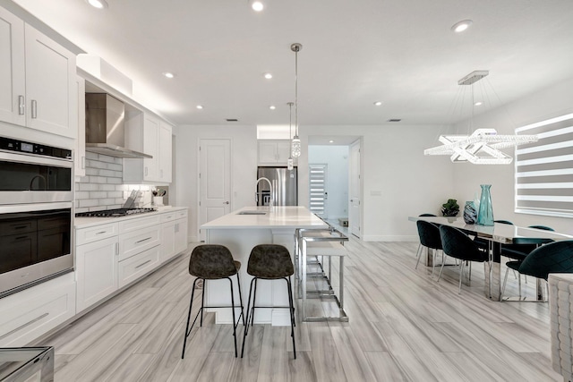 kitchen featuring a breakfast bar area, decorative light fixtures, stainless steel appliances, a kitchen island with sink, and white cabinets