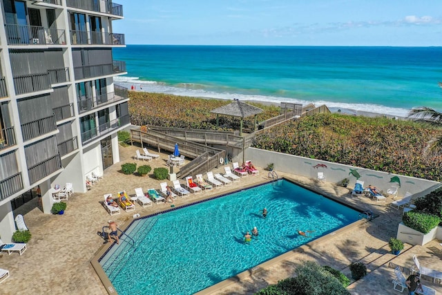 view of pool featuring a patio, a beach view, and a water view