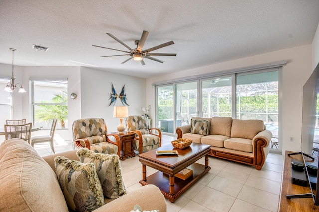 tiled living room with ceiling fan with notable chandelier and a textured ceiling