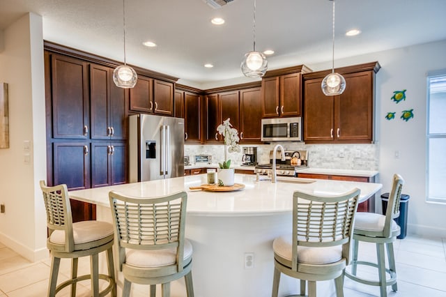 kitchen featuring an island with sink, appliances with stainless steel finishes, pendant lighting, and a kitchen breakfast bar