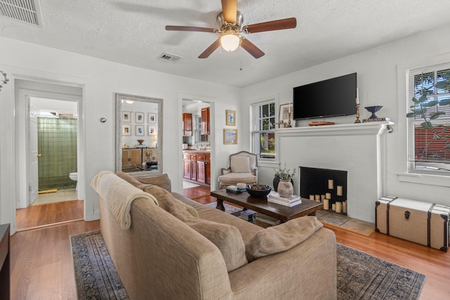 living room with ceiling fan, a textured ceiling, and light hardwood / wood-style floors