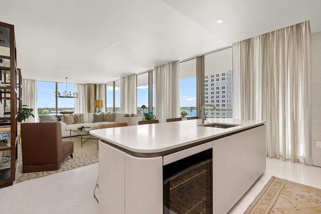 kitchen with a sink, wine cooler, light countertops, white cabinets, and a kitchen island with sink