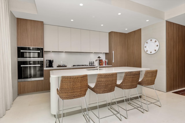 kitchen with a kitchen breakfast bar, an island with sink, dobule oven black, and light countertops