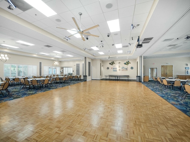 workout area featuring a drop ceiling, ceiling fan with notable chandelier, light parquet flooring, and a high ceiling