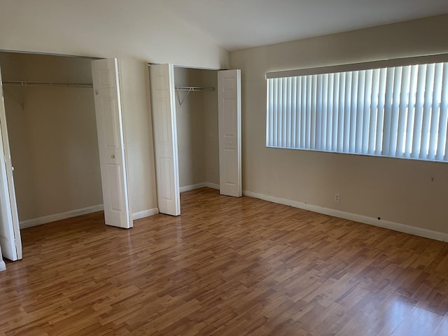 unfurnished bedroom with hardwood / wood-style flooring, vaulted ceiling, and two closets