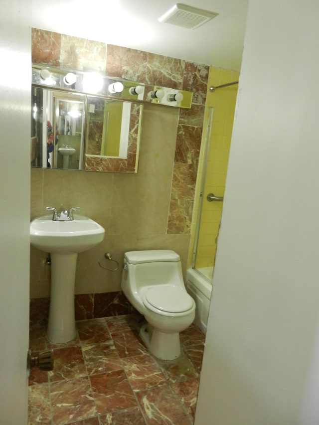 full bathroom with toilet, tiled shower / bath combo, sink, and tile walls