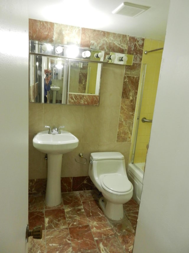 full bathroom with sink, combined bath / shower with glass door, tile walls, tasteful backsplash, and toilet