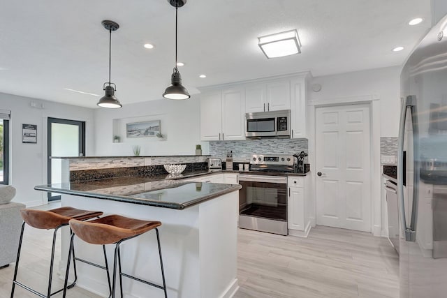 kitchen with dark stone countertops, pendant lighting, stainless steel appliances, decorative backsplash, and white cabinets