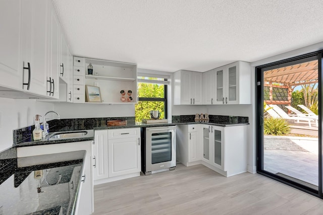 kitchen with wine cooler, dark stone countertops, sink, and white cabinets