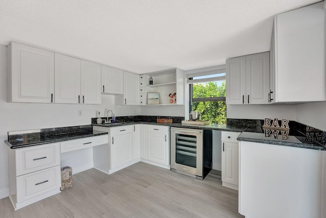 kitchen with wine cooler, sink, white cabinetry, a textured ceiling, and light wood-type flooring