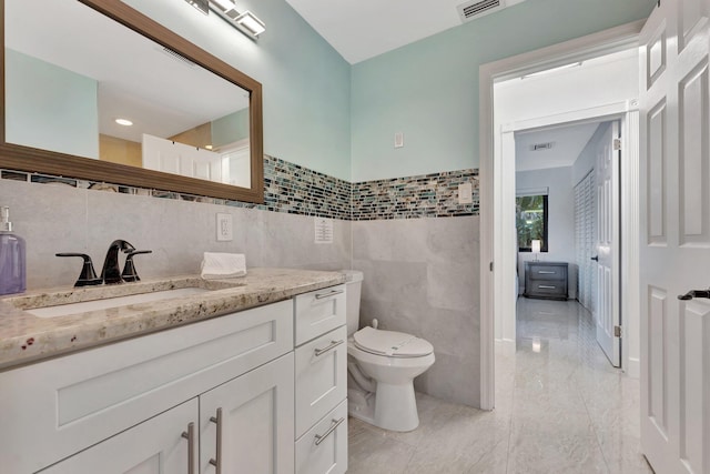 bathroom with vanity, tile walls, and toilet