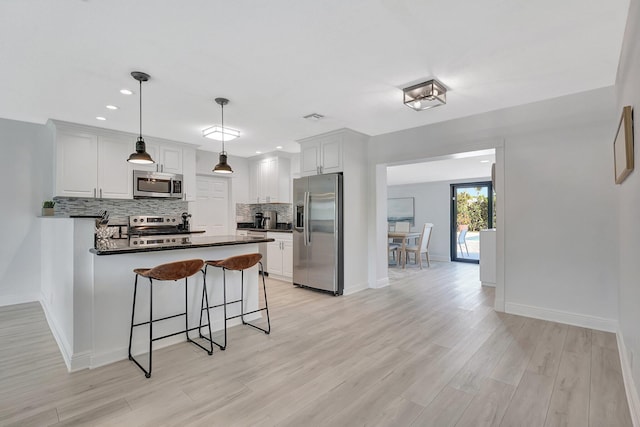 kitchen with appliances with stainless steel finishes, white cabinets, backsplash, and decorative light fixtures