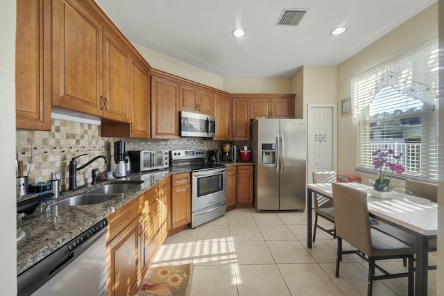 kitchen featuring sink, light tile patterned floors, stainless steel appliances, tasteful backsplash, and dark stone counters