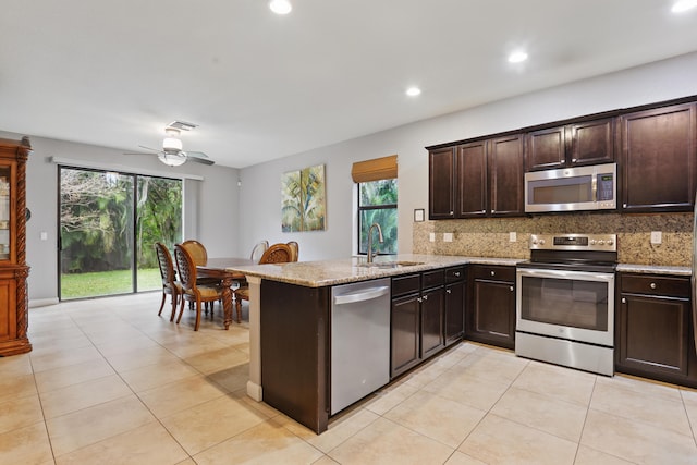 kitchen with sink, decorative backsplash, light stone counters, kitchen peninsula, and stainless steel appliances