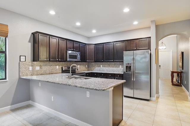 kitchen featuring dark brown cabinetry, sink, light stone counters, appliances with stainless steel finishes, and kitchen peninsula