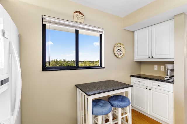 kitchen with white refrigerator with ice dispenser, a breakfast bar, white cabinets, and light wood-type flooring