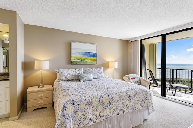 bedroom with a wall of windows, access to exterior, a water view, a textured ceiling, and light colored carpet