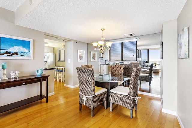 dining space with a textured ceiling, an inviting chandelier, and light hardwood / wood-style flooring