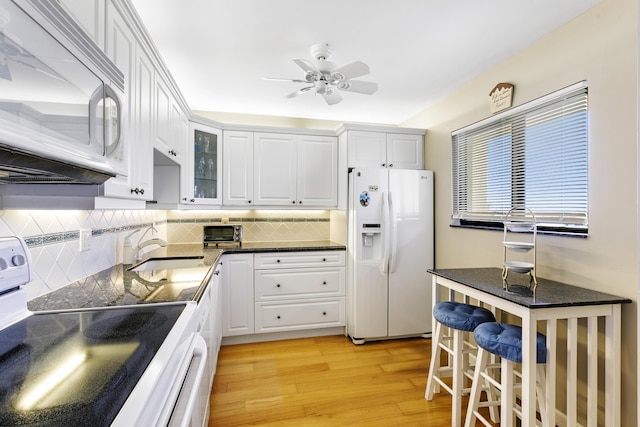 kitchen with tasteful backsplash, sink, white cabinets, white appliances, and light wood-type flooring