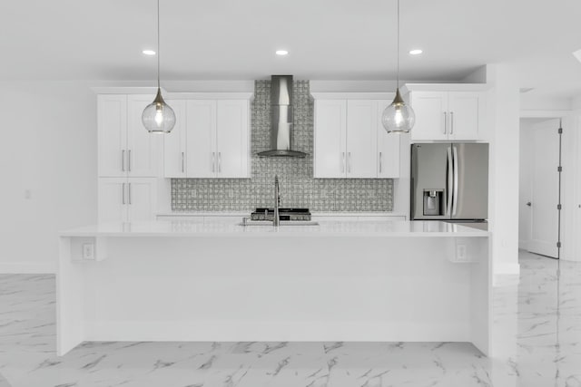 kitchen with pendant lighting, wall chimney exhaust hood, stainless steel appliances, and a kitchen island with sink