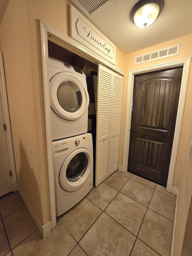 laundry room featuring light tile patterned floors, a textured ceiling, and stacked washer / dryer