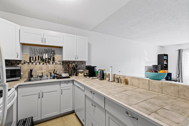 kitchen with sink, backsplash, tile counters, white appliances, and a textured ceiling