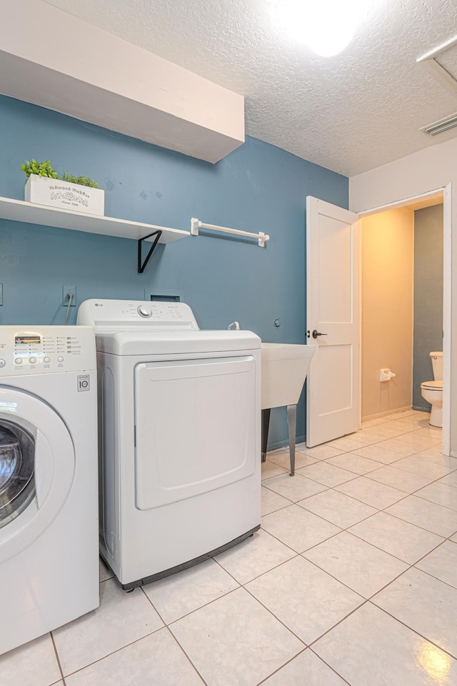 laundry area with light tile patterned floors, washing machine and clothes dryer, and a textured ceiling