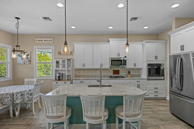 kitchen featuring sink, appliances with stainless steel finishes, white cabinetry, hanging light fixtures, and light stone counters