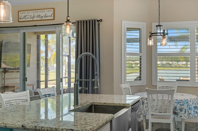 kitchen featuring a kitchen island with sink, light stone countertops, sink, and hanging light fixtures